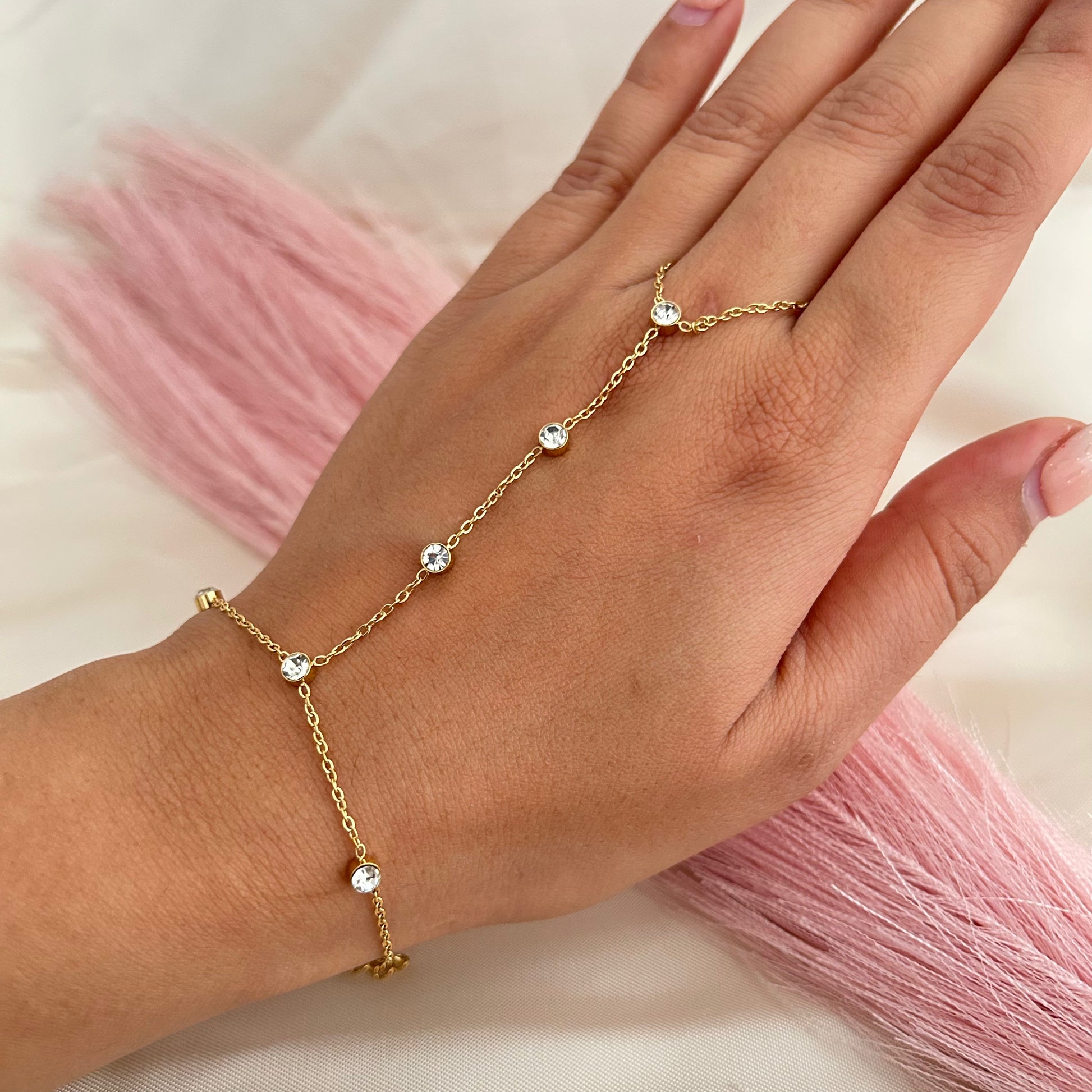 Minimal gold hand chain with small round stones connecting finger and wrist